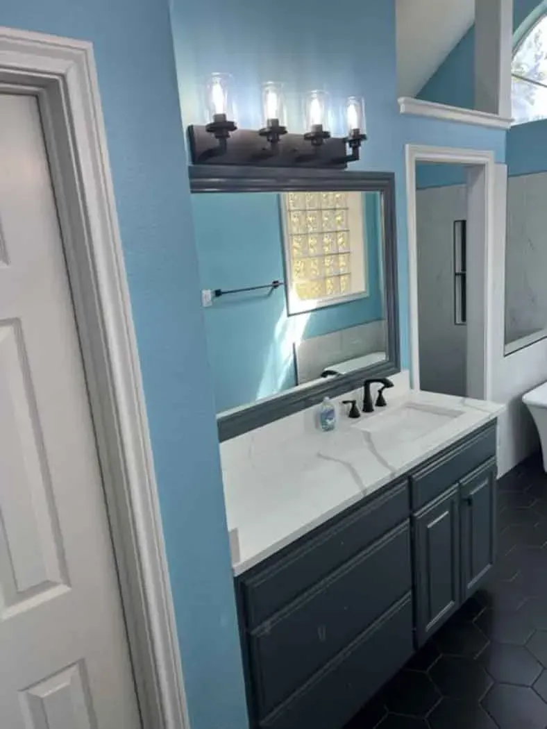 Bathroom with blue walls, gray vanity, and white countertop. A mirror and light fixture are above the sink.
