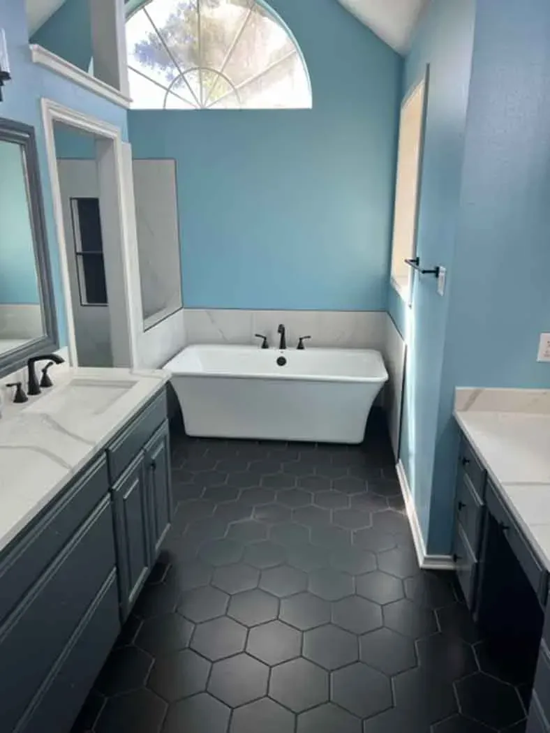 Bathroom with blue walls, dark hexagonal tile floor, white tub, and gray vanity with marble countertop.