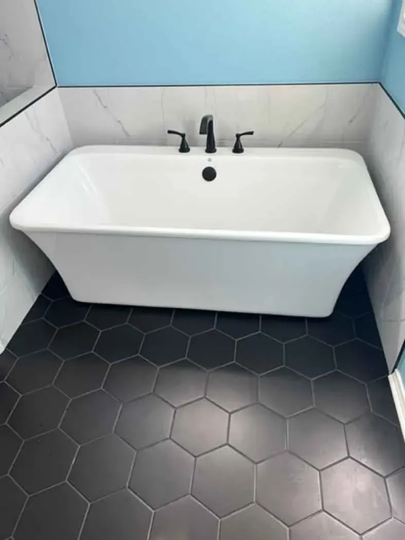 White bathtub with black faucet, black hexagon tile floor, and light blue wall.
