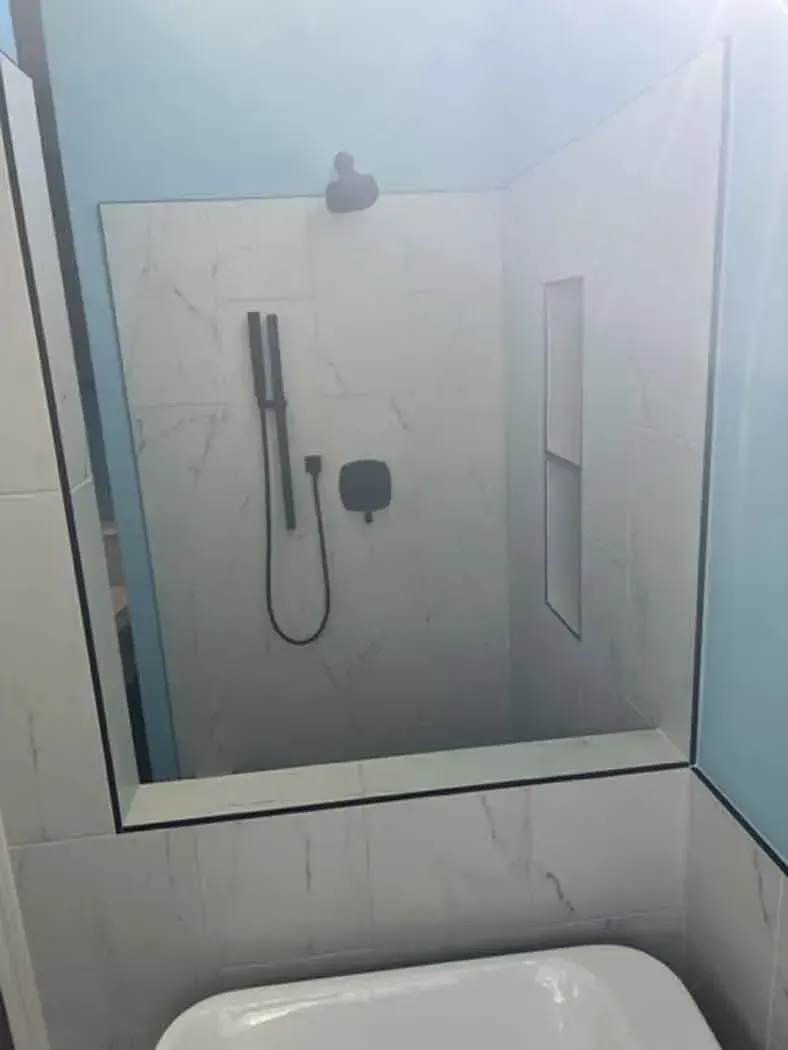 Modern shower with black fixtures and built-in shelving, white marble-look tiles.