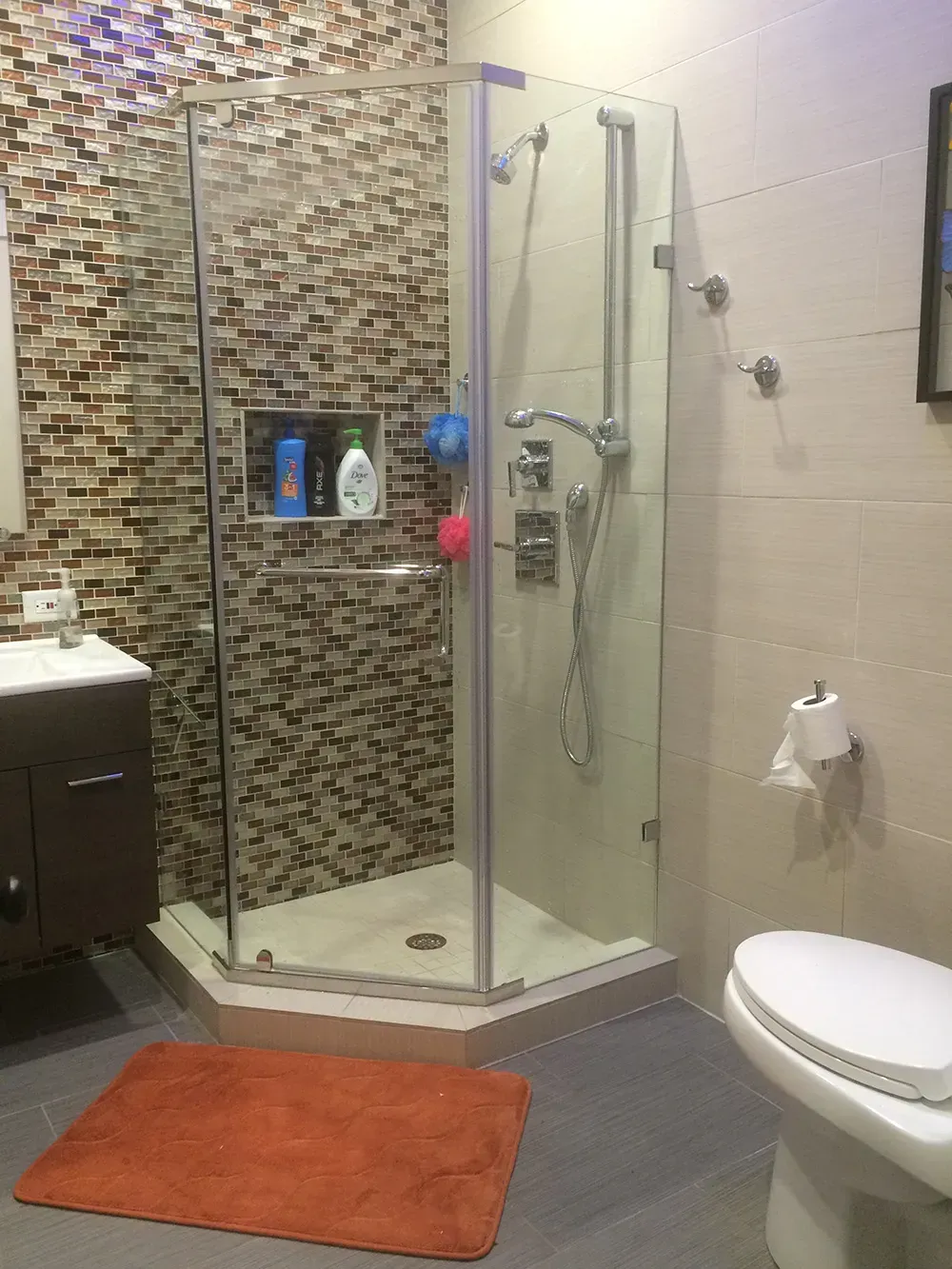 Bathroom with corner shower, patterned tile accent wall, orange rug, and toilet.