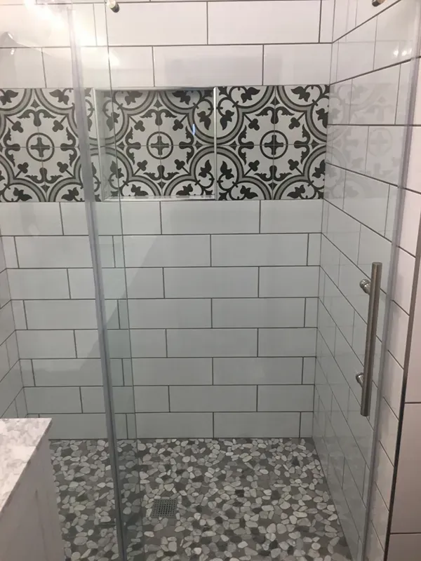 Shower stall with pebble floor, white subway tile walls, and decorative patterned tile border. Glass door.