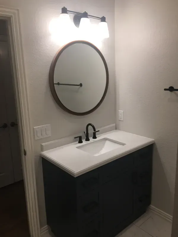 Bathroom with dark blue vanity, white countertop, round mirror, and black faucet.
