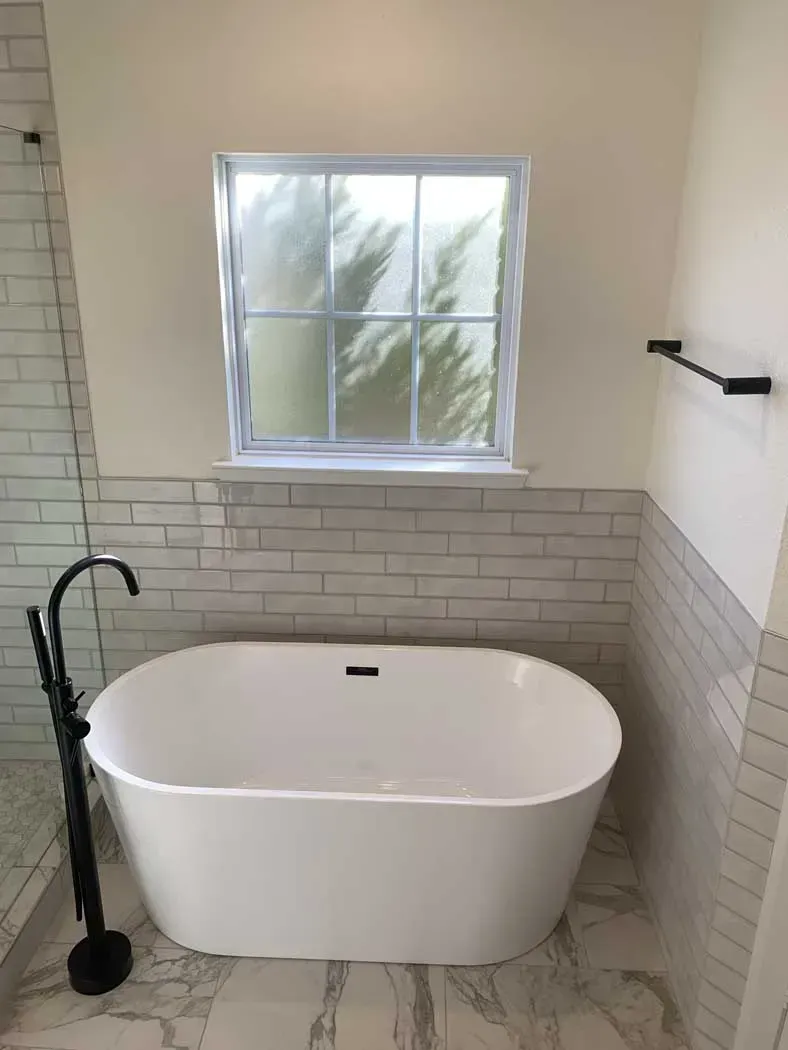 Bathroom with white oval tub, white subway tile, and window with frosted glass.