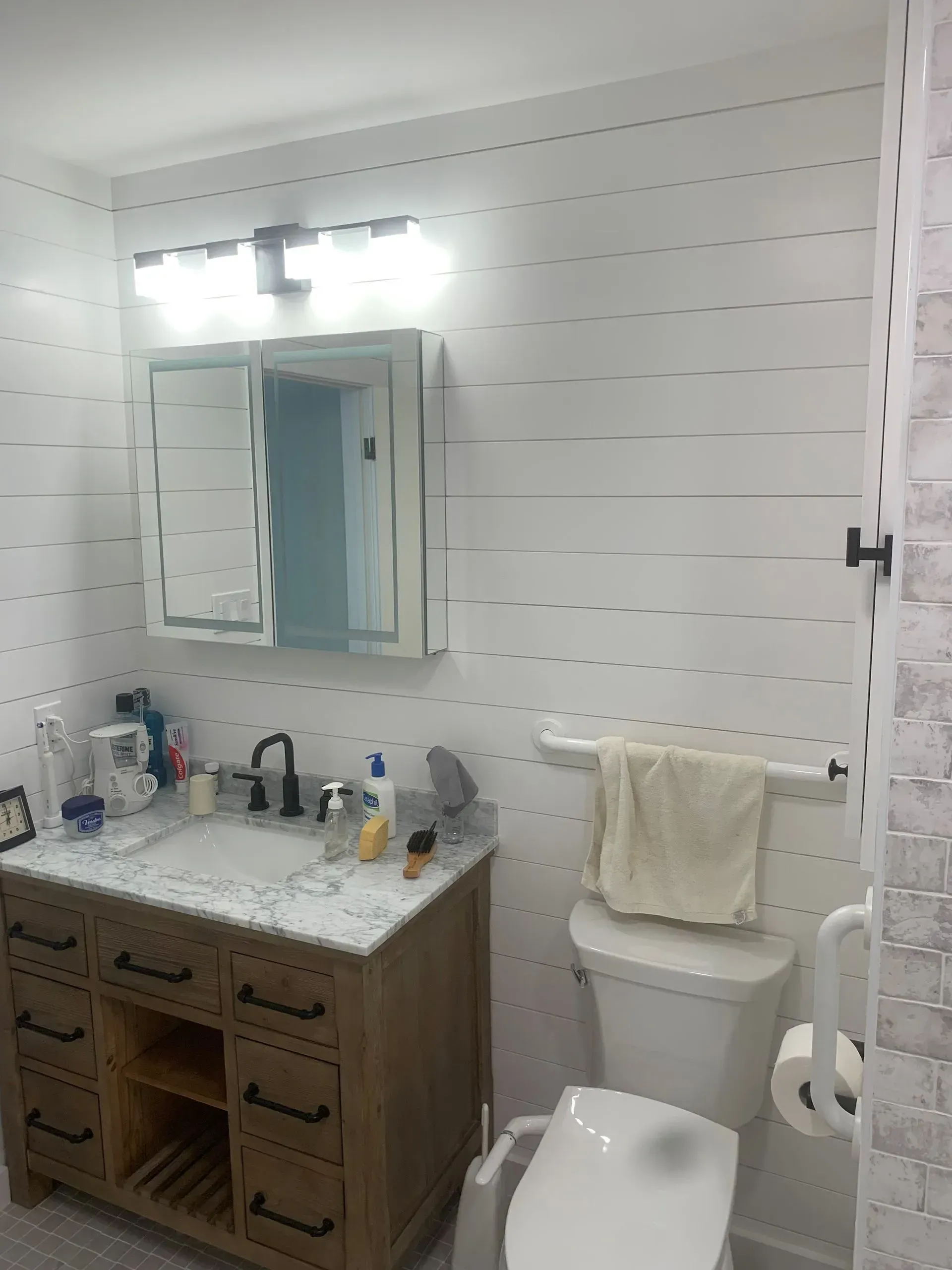 Bathroom with wood vanity, white toilet, tiled walls, and mirror.