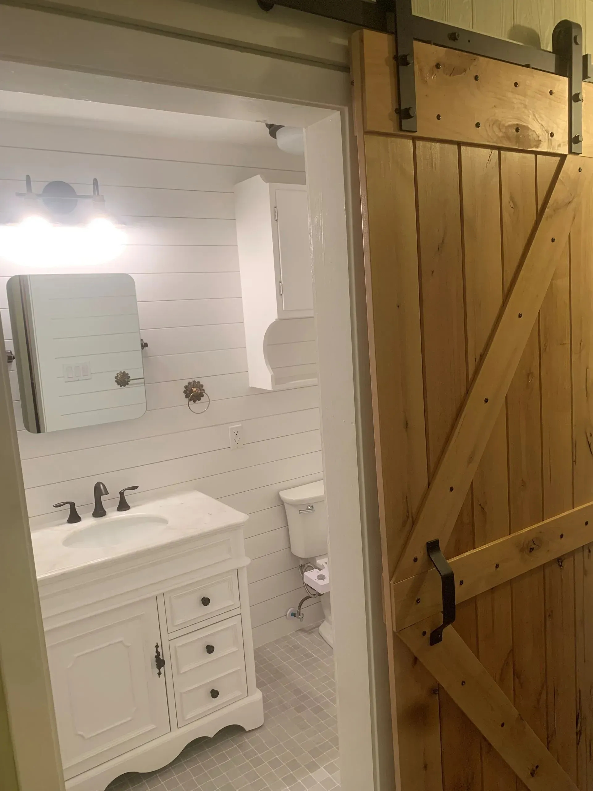 Barn door opens to a white-tiled bathroom with a vanity, mirror, and toilet.