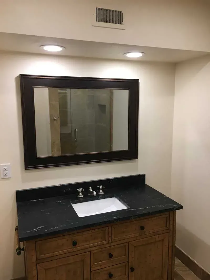 Bathroom vanity with a dark countertop, wooden cabinet, large mirror, and recessed lighting.