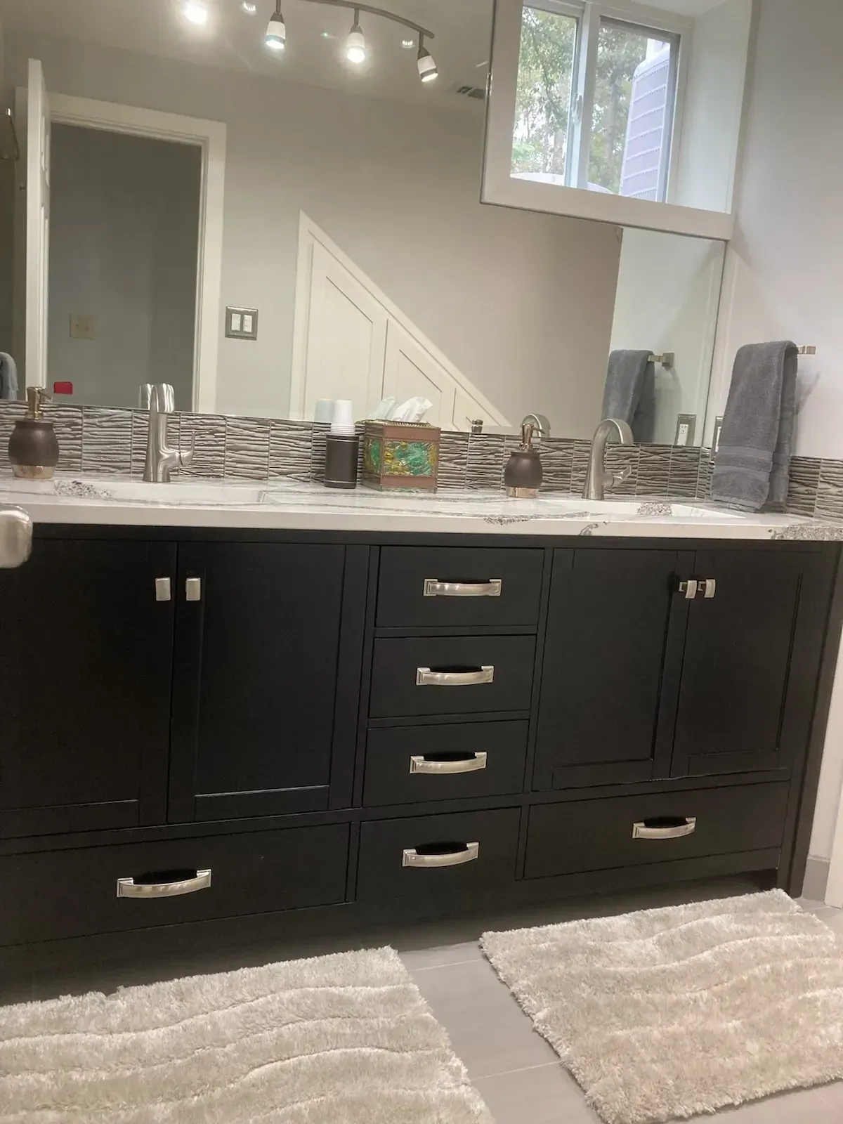 Black double-sink bathroom vanity with light countertops, mosaic tile backsplash, two mirrors, and gray floor.