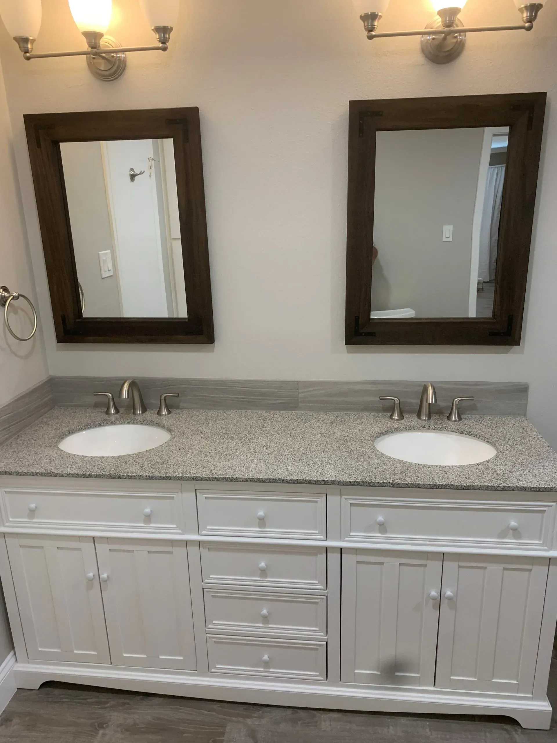 Bathroom with two sinks, white vanity, granite countertop, brown-framed mirrors, and silver fixtures.