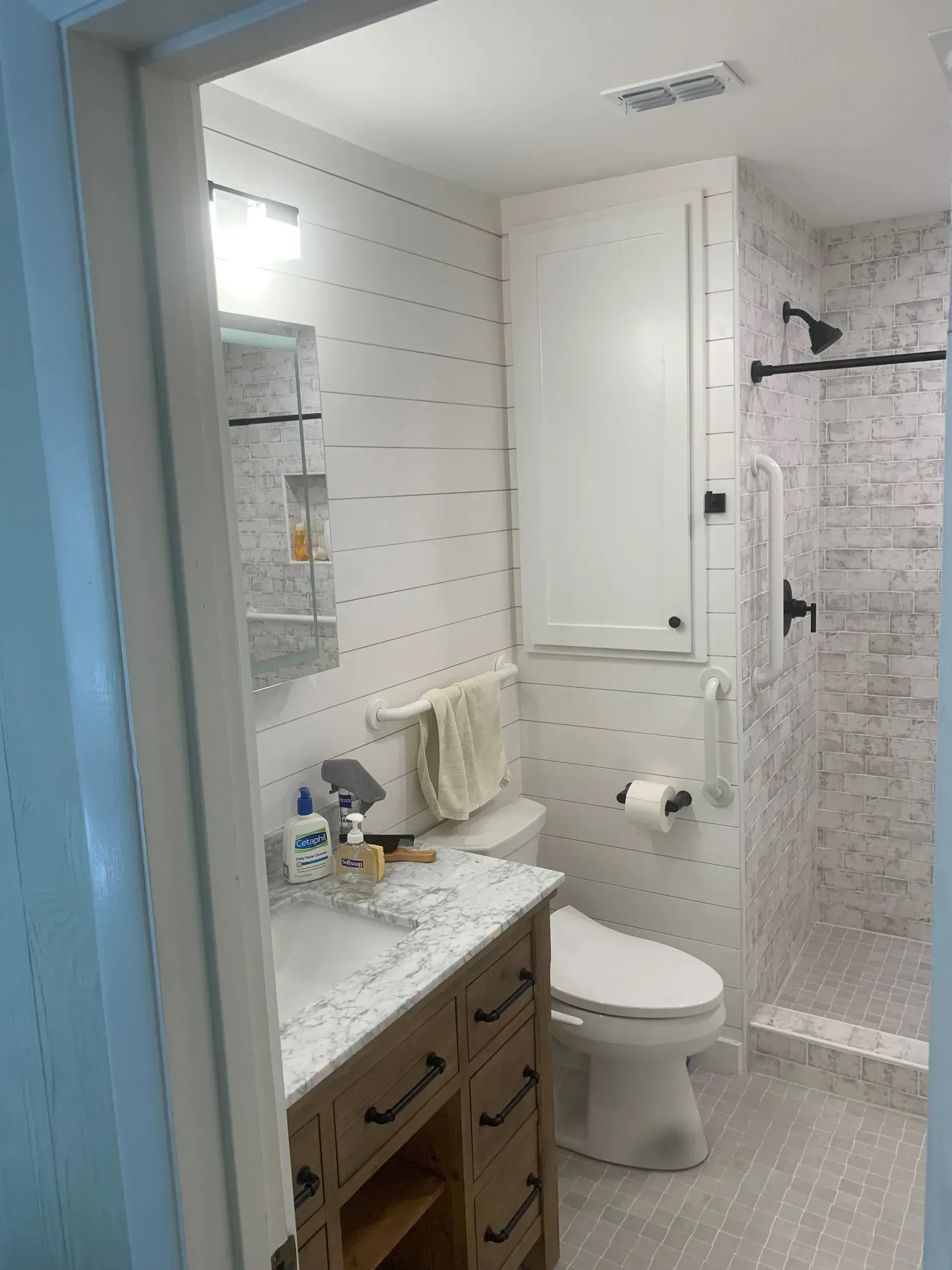 Modern white bathroom with vanity, toilet, and shower. White shiplap walls, marble-look countertop.