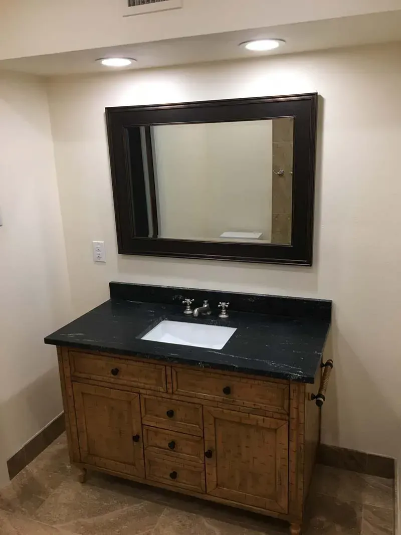 Bathroom with wooden vanity, dark countertop, and large mirror.