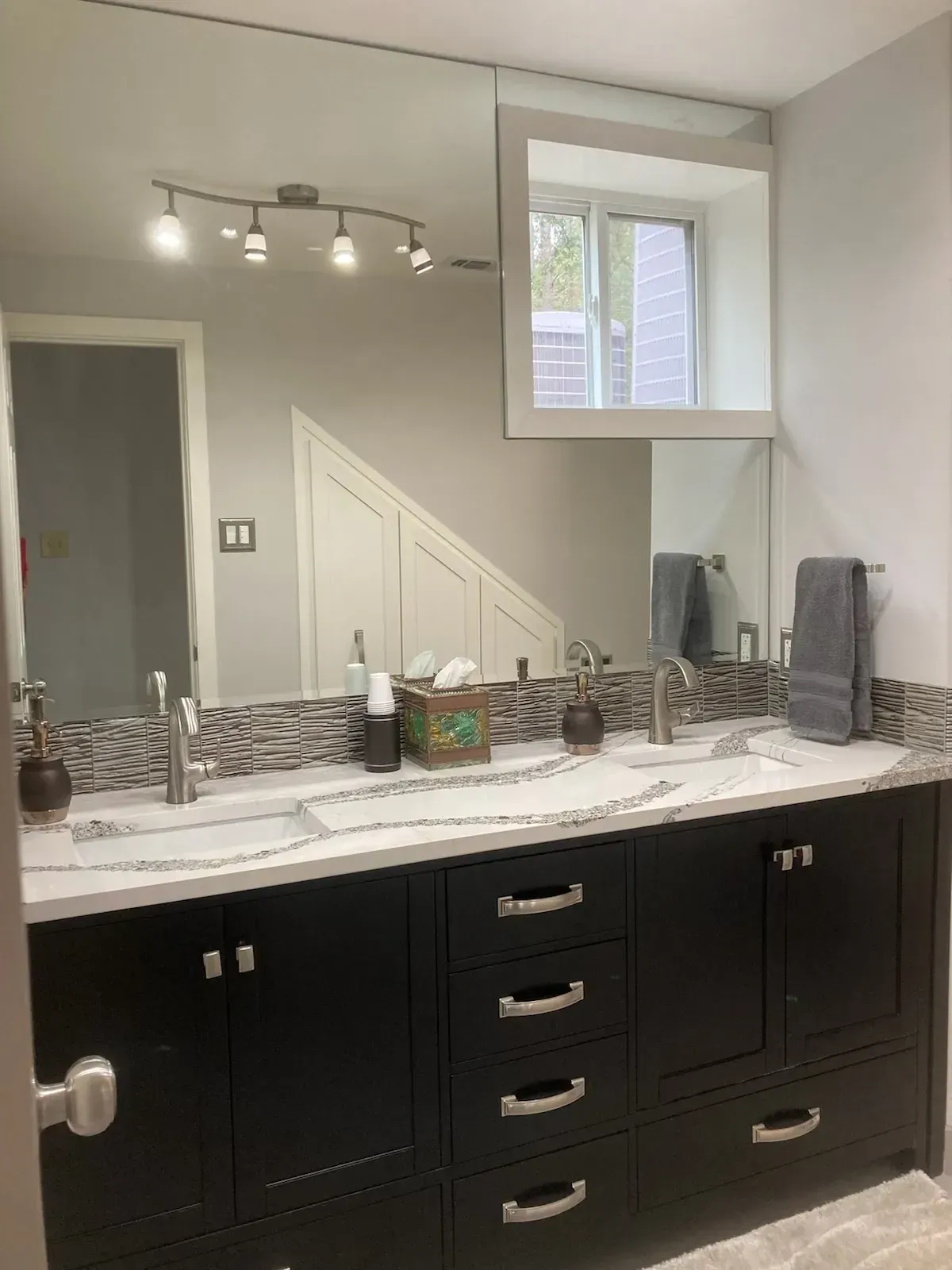 Double vanity bathroom with black cabinets, white countertop, and large mirror.