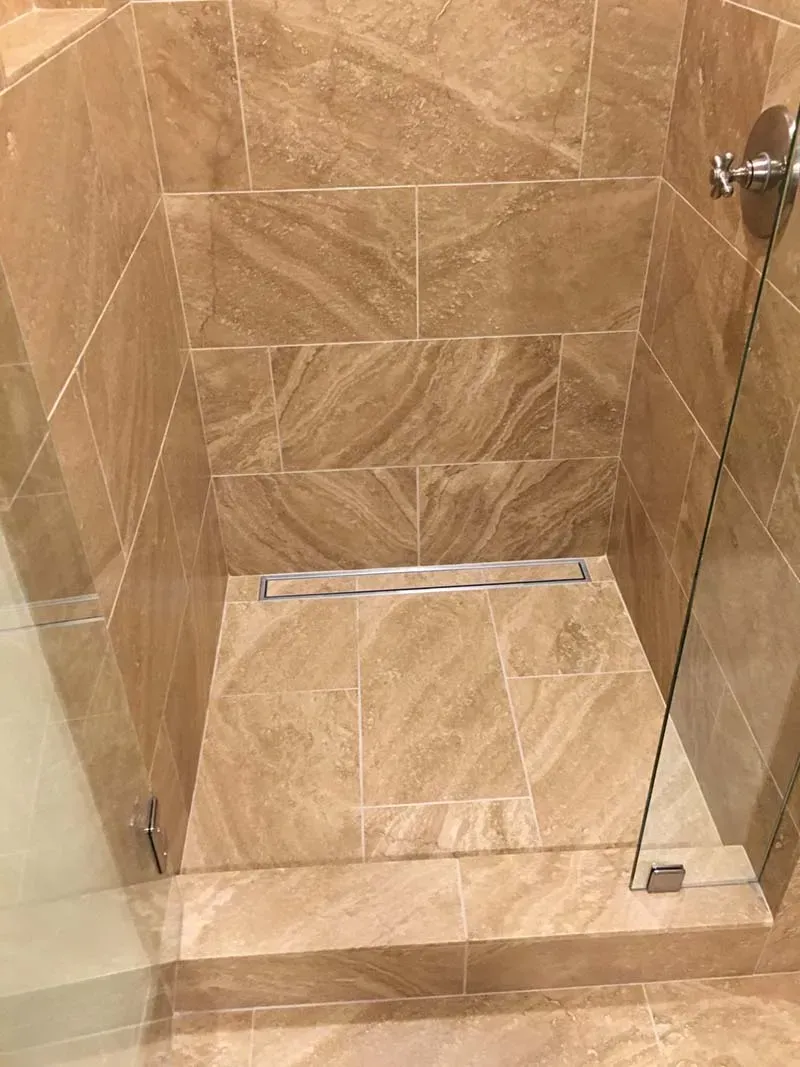 Shower stall with brown marble tile and a linear drain.