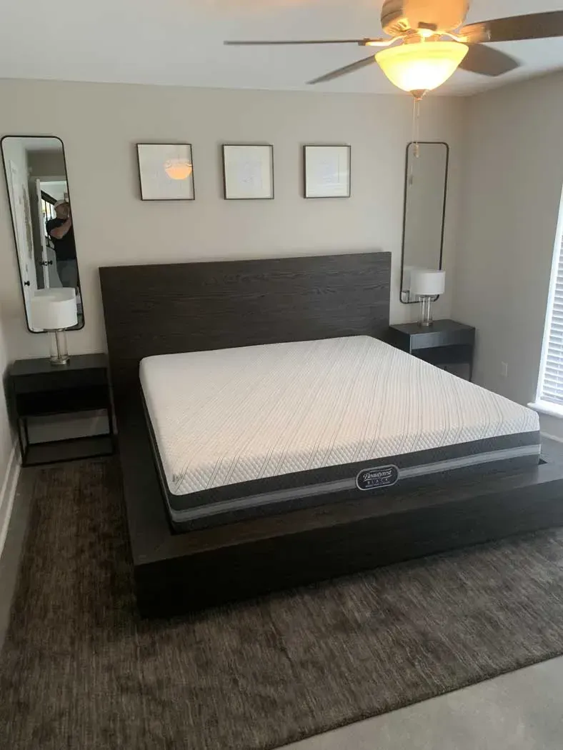 Bedroom with a bed, nightstands, mirrors, and framed artwork. The room has neutral colors.