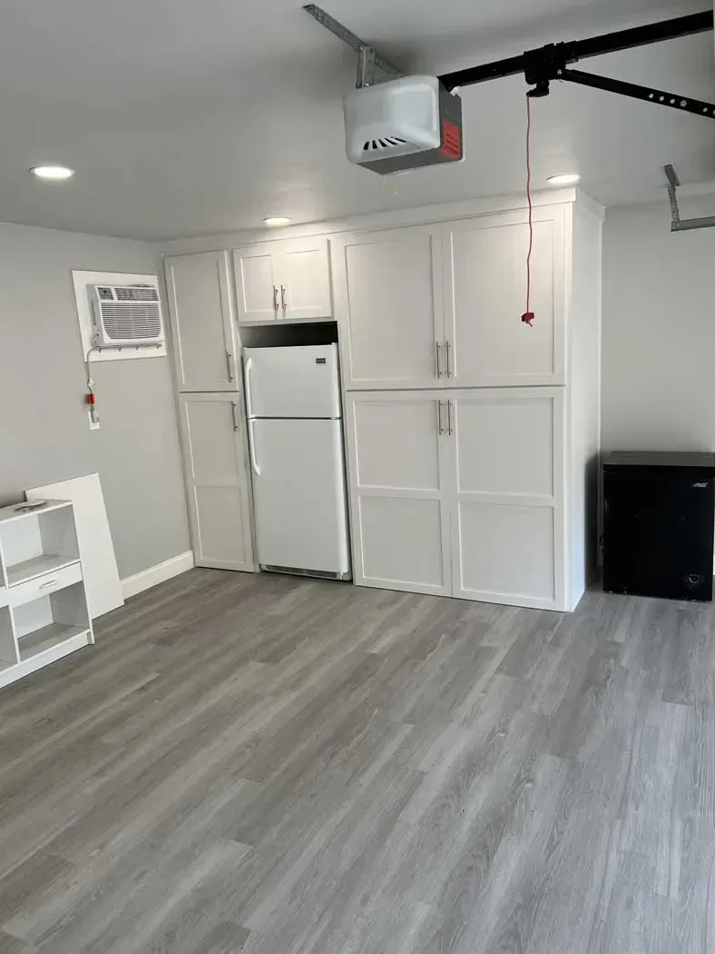 Garage with white cabinets, refrigerator, and gray flooring.