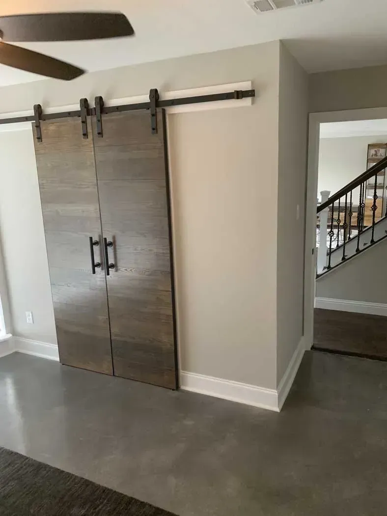 Barn doors on track against a light gray wall, transitioning to an entryway with stairs.