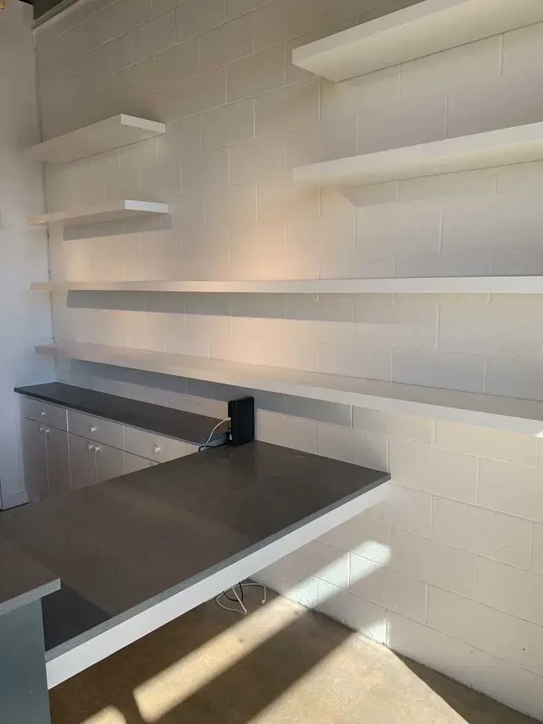 White shelves on a white block wall above a gray counter. Sunlight streams in.