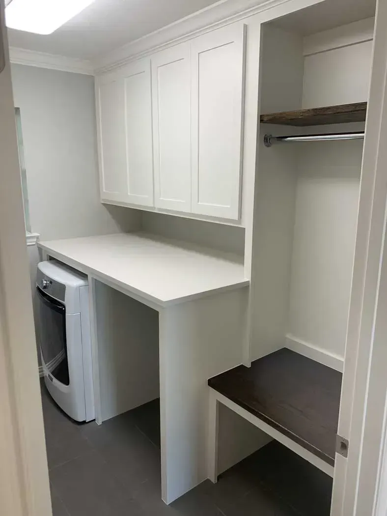 Laundry room with white cabinets, countertop, and washer.  A bench and hanging rod are in a side alcove.