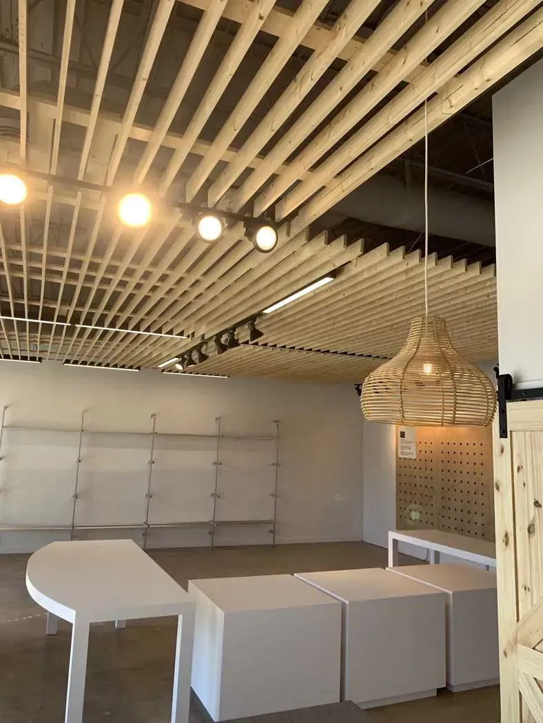 Empty retail space with light wood slat ceiling, shelves, and white display tables.