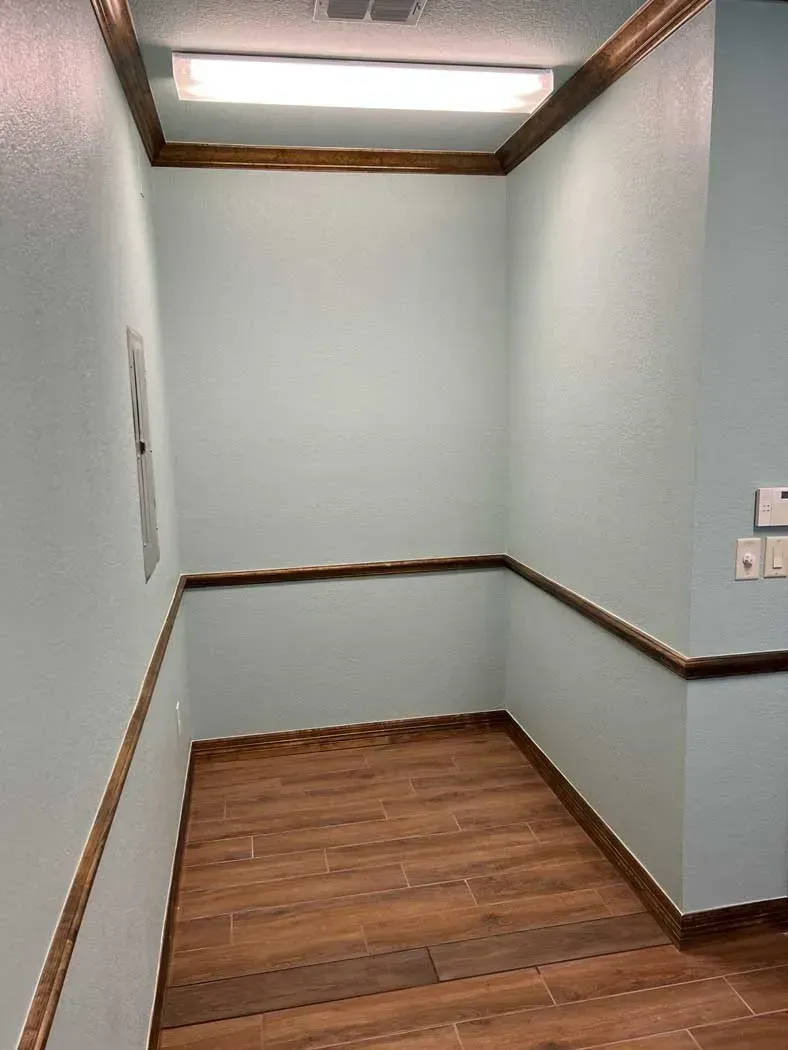 Small room with wood trim and flooring, blue walls, a fluorescent light, and electrical panel.