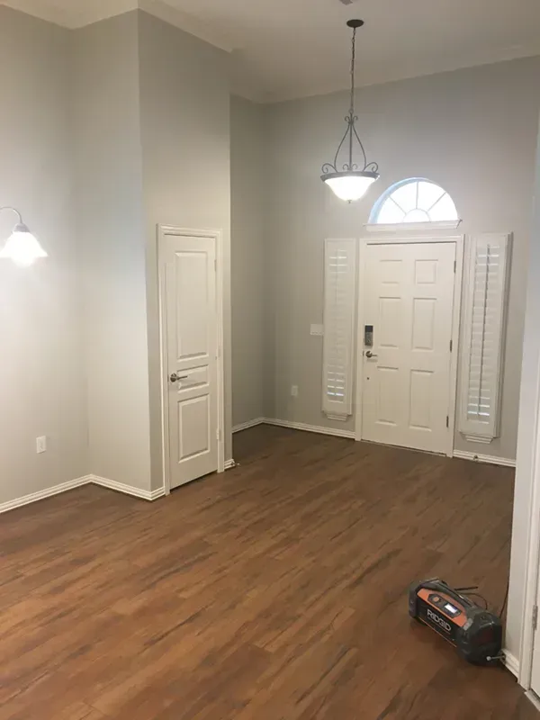 Empty room with light gray walls, wood-look flooring, white door, and hanging light fixture.