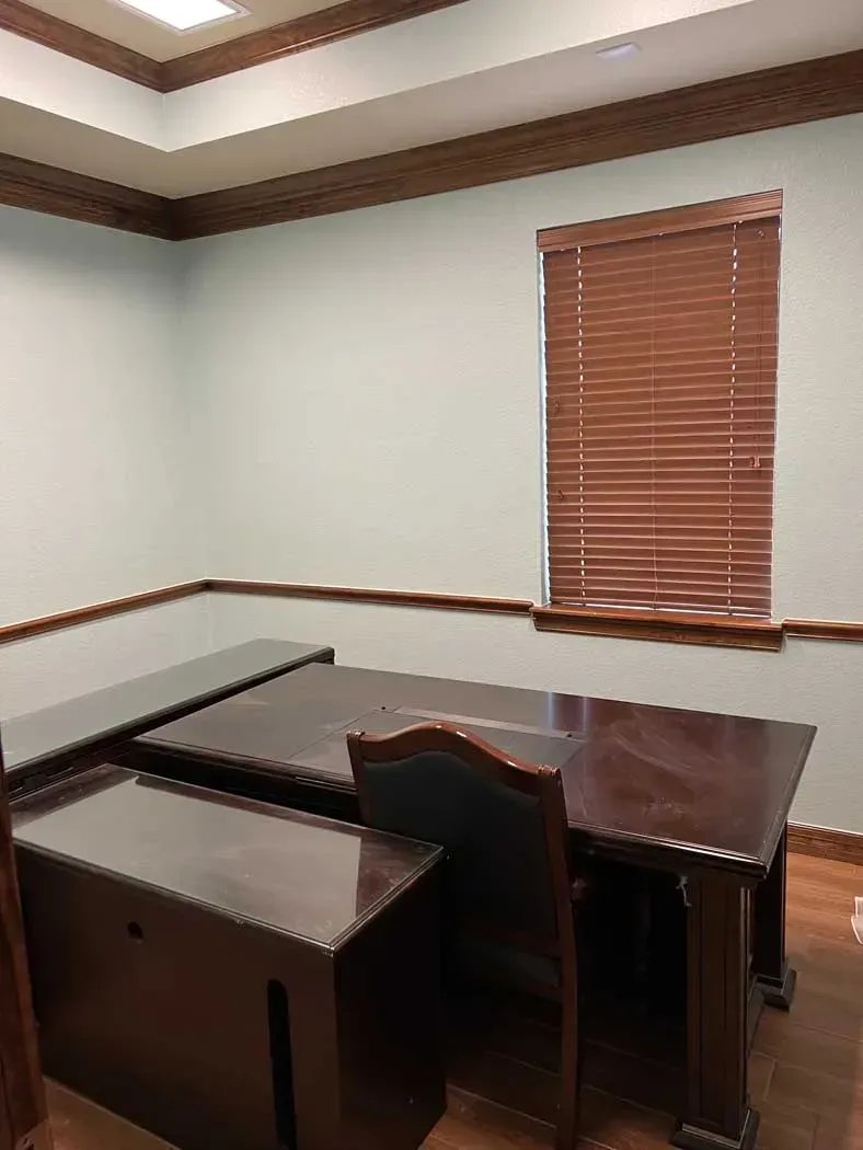 Office with wooden furniture, blue-green walls, and a window with blinds.