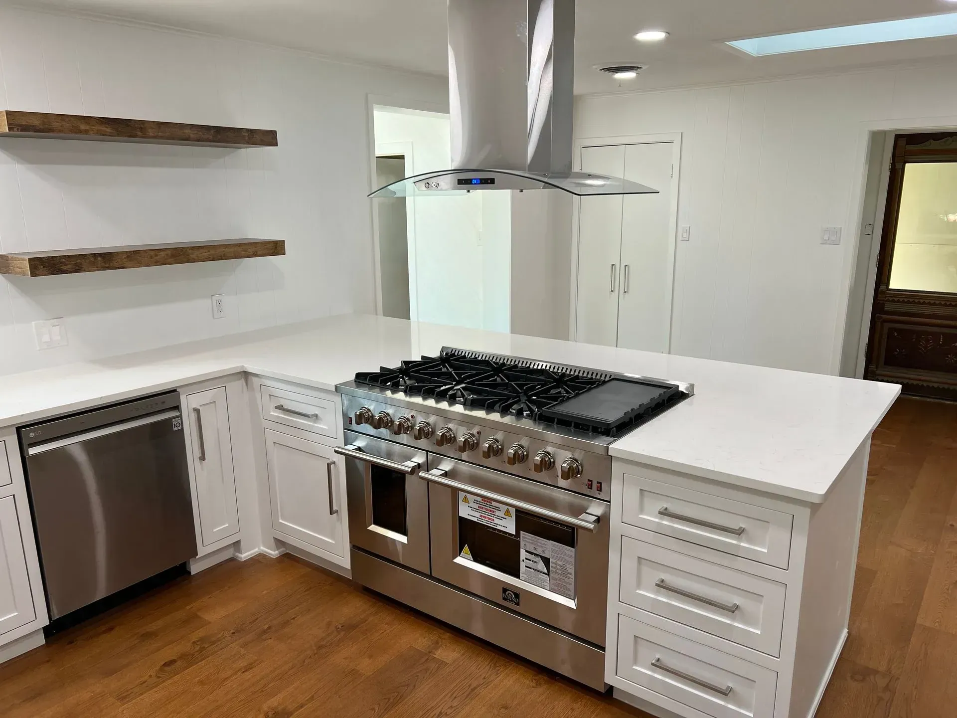 Modern white kitchen with stainless steel appliances, butcher block shelving, and hardwood floors.