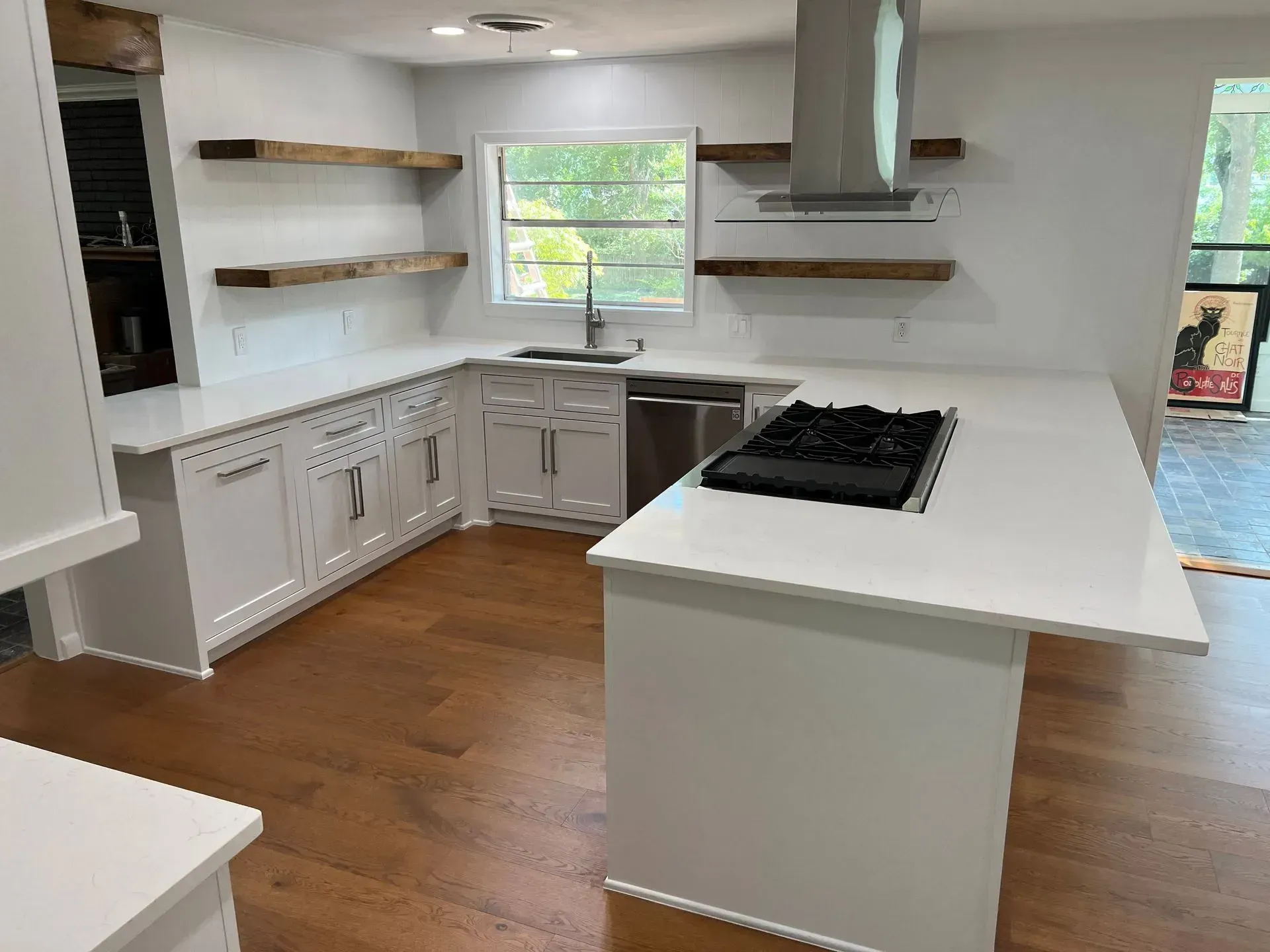 Modern kitchen with white cabinets, countertops, wood shelves, and a gas cooktop on an island.
