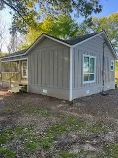 Gray cottage with porch and vertical siding, white trim, and a small yard.