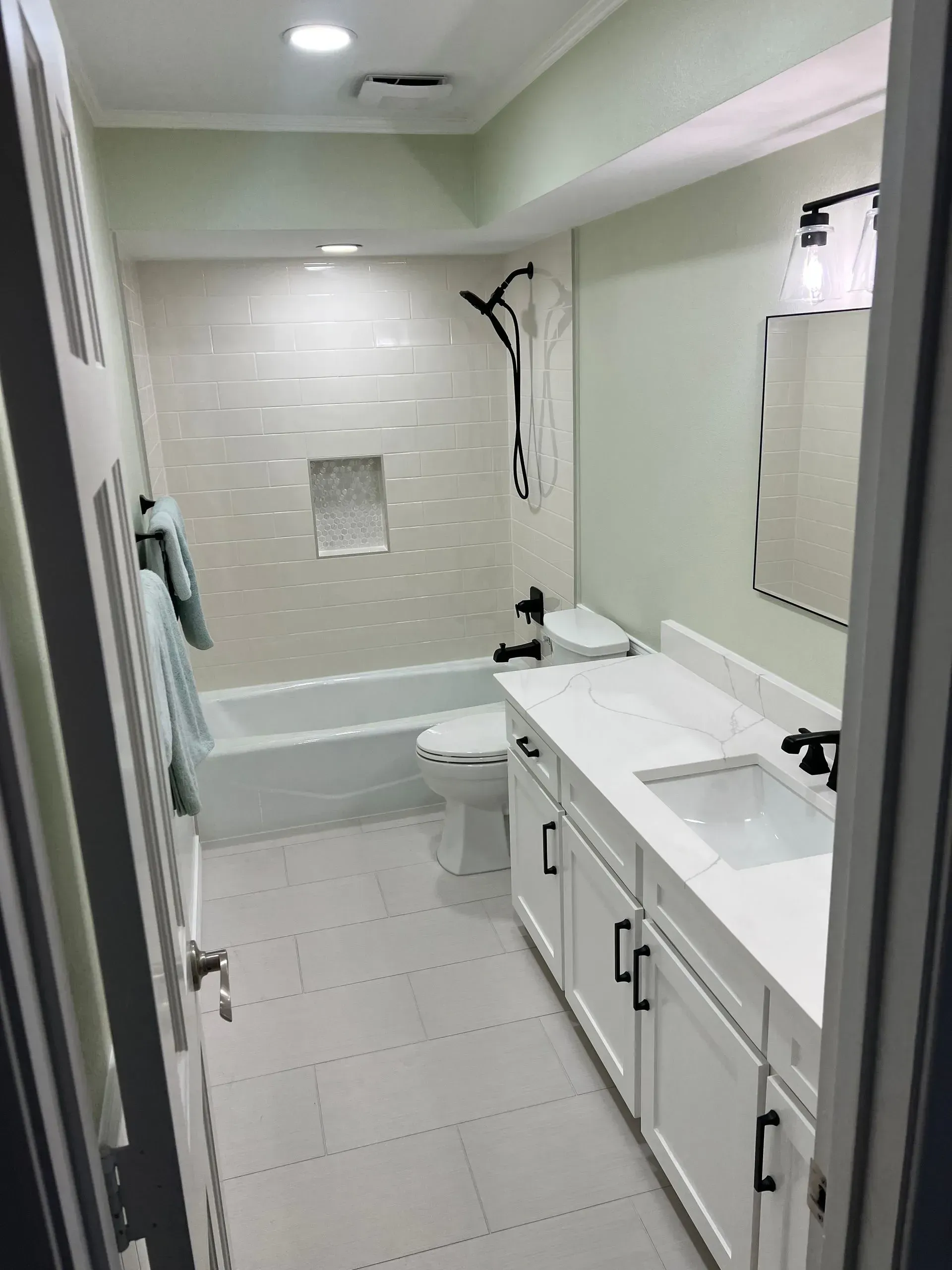 Bathroom with white cabinets, tub, and tile; black fixtures.
