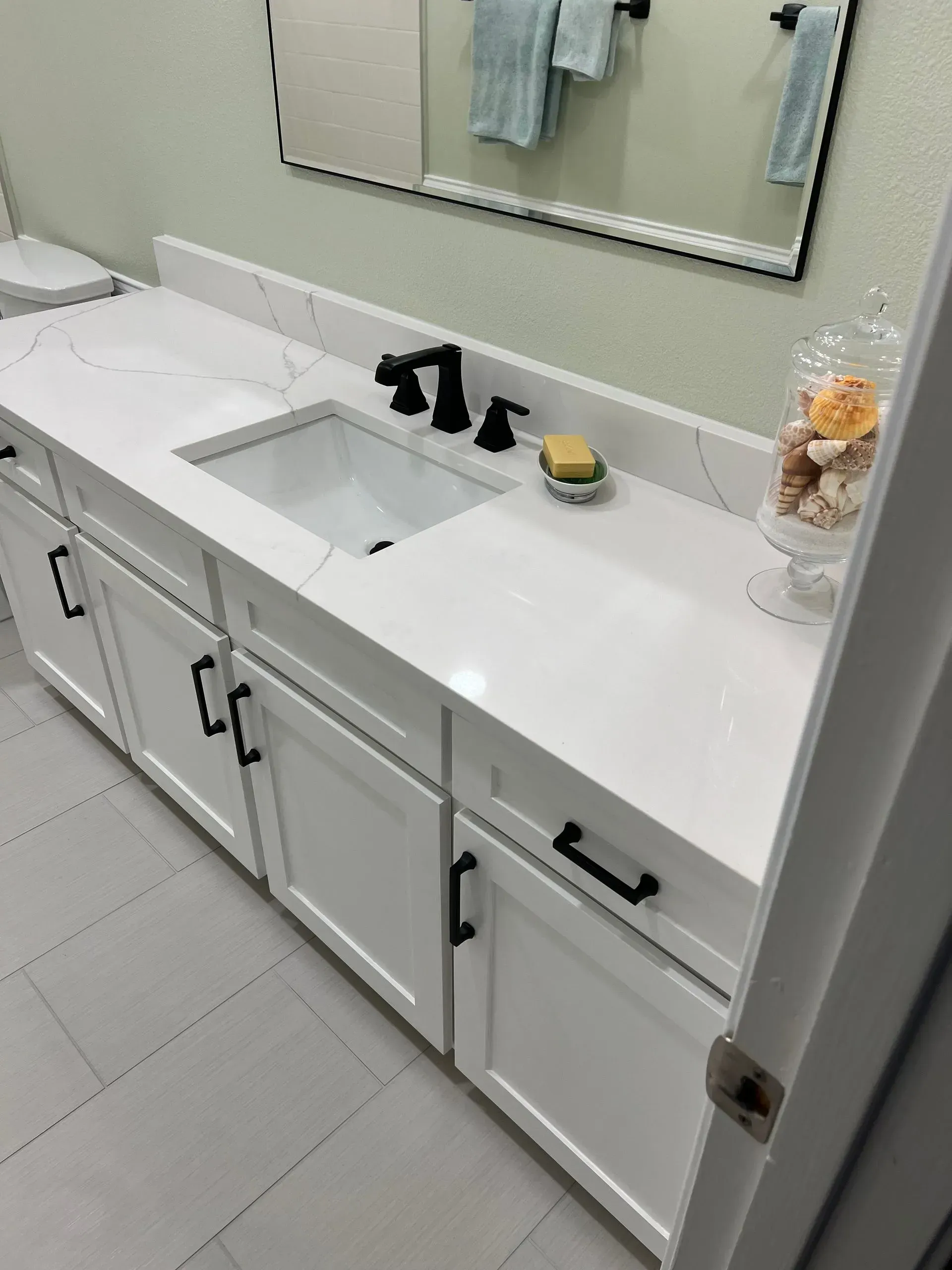 White bathroom vanity with black hardware, white countertop, and rectangular mirror.