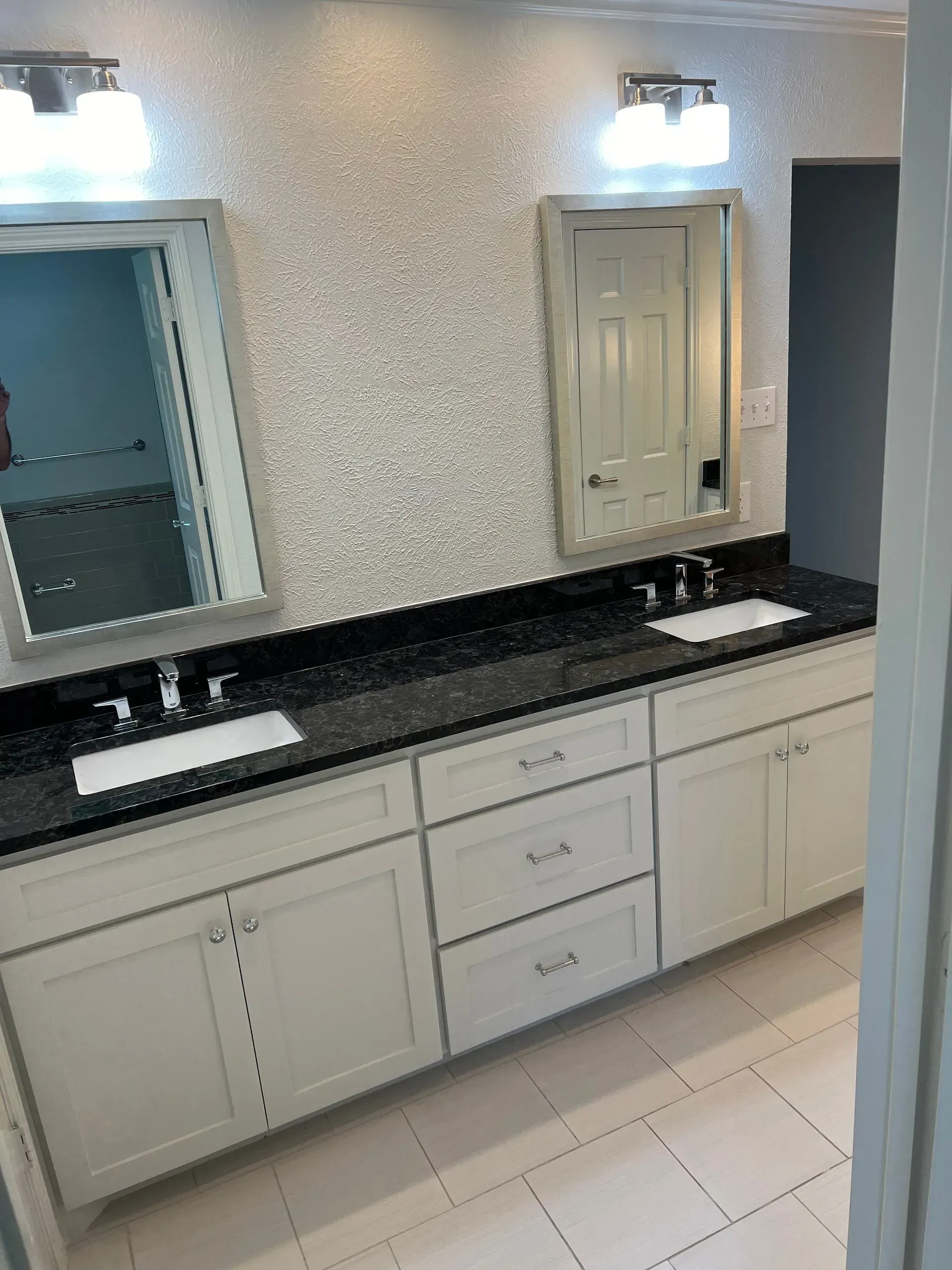 Bathroom with two sinks, white cabinets, black countertop, mirrors, and sparkly wall tile.
