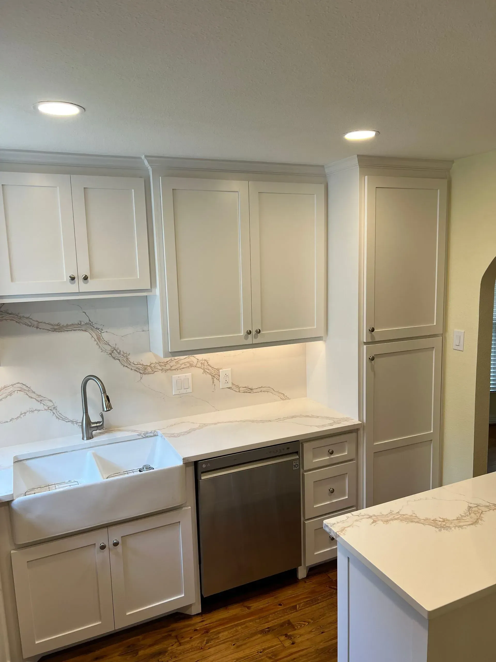 White kitchen with cabinets, stainless steel dishwasher, and quartz countertop.