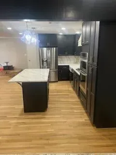 Modern kitchen with dark cabinetry, stainless steel appliances, and a marble countertop island.