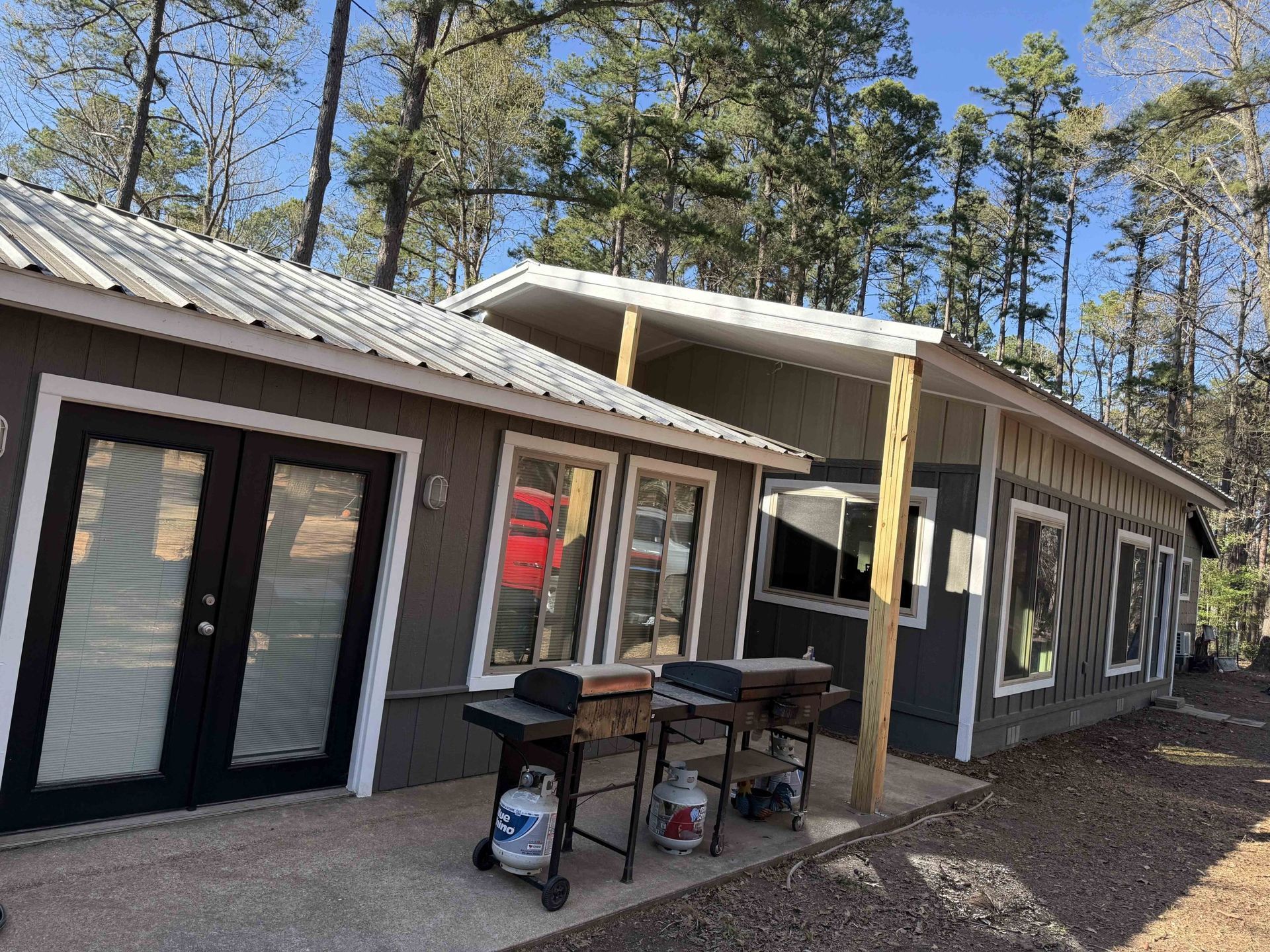 Cabin with dark gray siding, white trim, and metal roof; two grills on the patio.