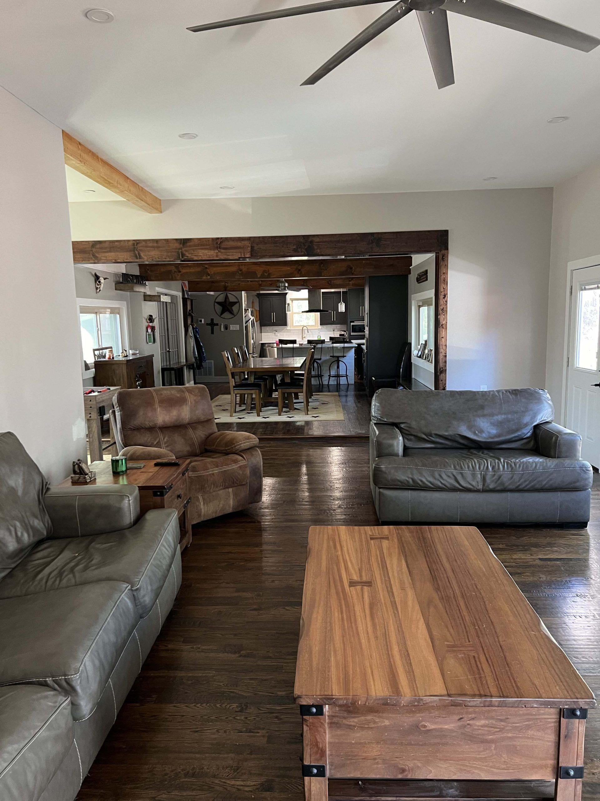 Living room with leather furniture and wood floors, open to a kitchen.