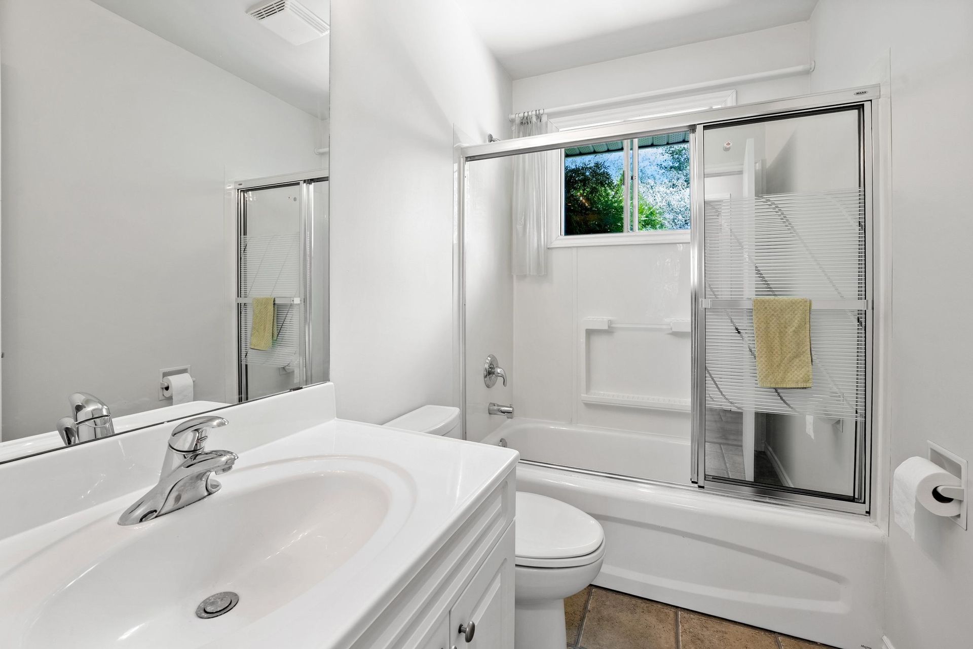 White bathroom with a sink, toilet, and shower/tub combo. A window lets in natural light.