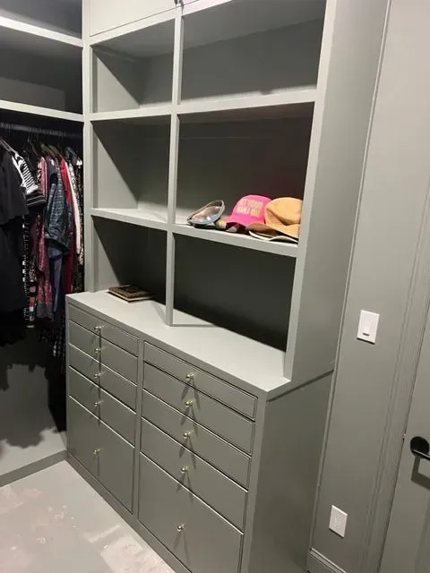 Closet with built-in shelves and drawers painted a light gray; clothes hanging on a rod.
