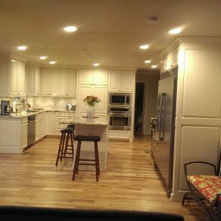 Spacious kitchen with white cabinets, stainless steel appliances, and wood flooring. Island with stools, recessed lighting.