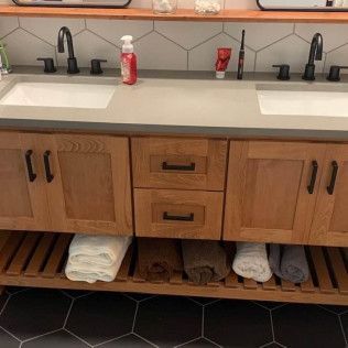 Wooden double bathroom vanity with sinks, faucets, and open shelf for towels.