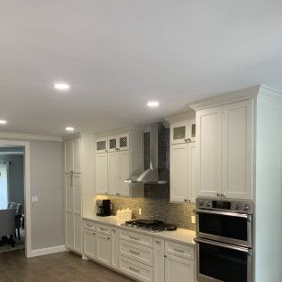White kitchen with stainless steel appliances and cabinetry; a gray backsplash, and recessed lighting.
