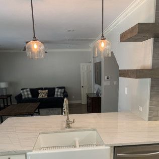 Kitchen with pendant lights over a countertop, sink, and view into living room with sofa.