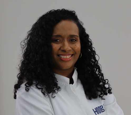 Veterinária de uniforme azul segurando um cachorrinho, sorrindo.