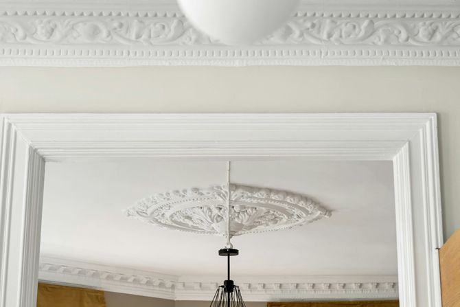 Decorative white ceiling molding and mirror above a hanging chandelier in a bright room