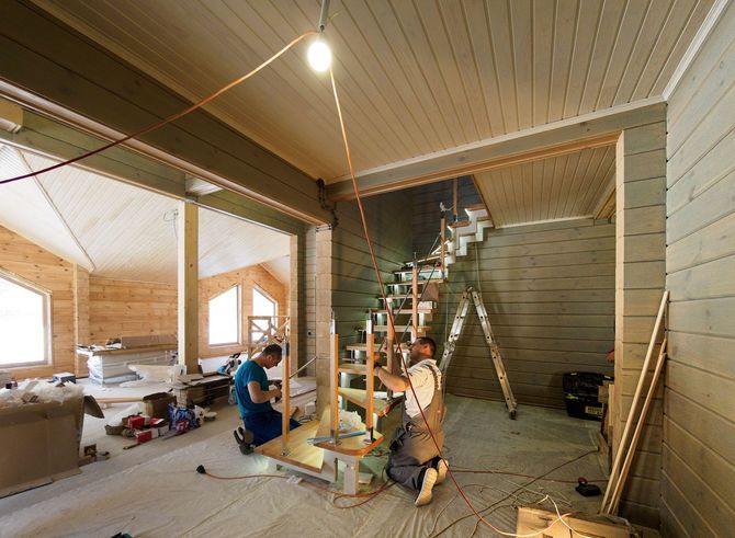 Workers installing a staircase inside a wood-paneled room under construction