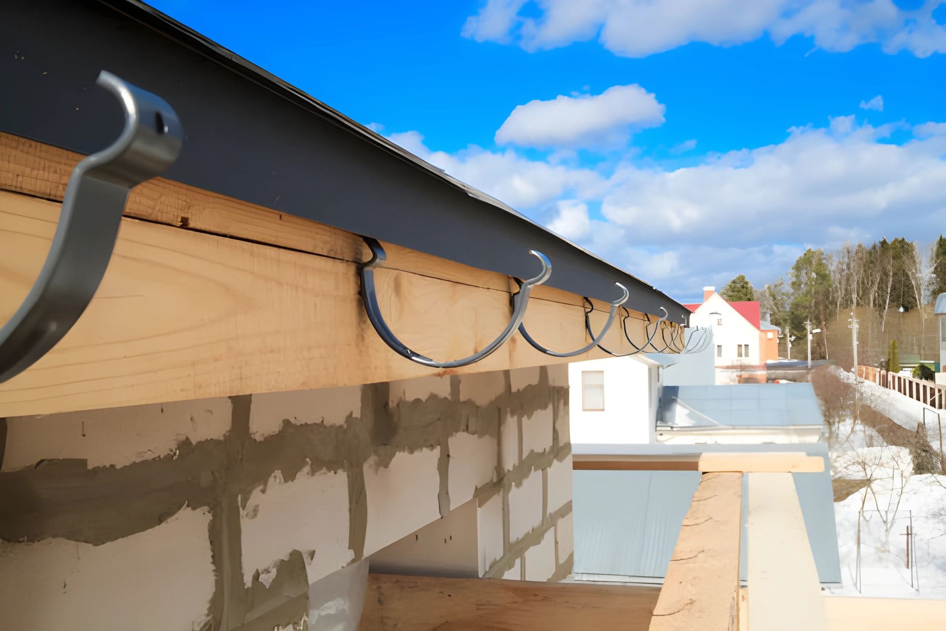 Close-up of a roof gutter system with metal brackets attached to the wooden structure, clear sky in the background.