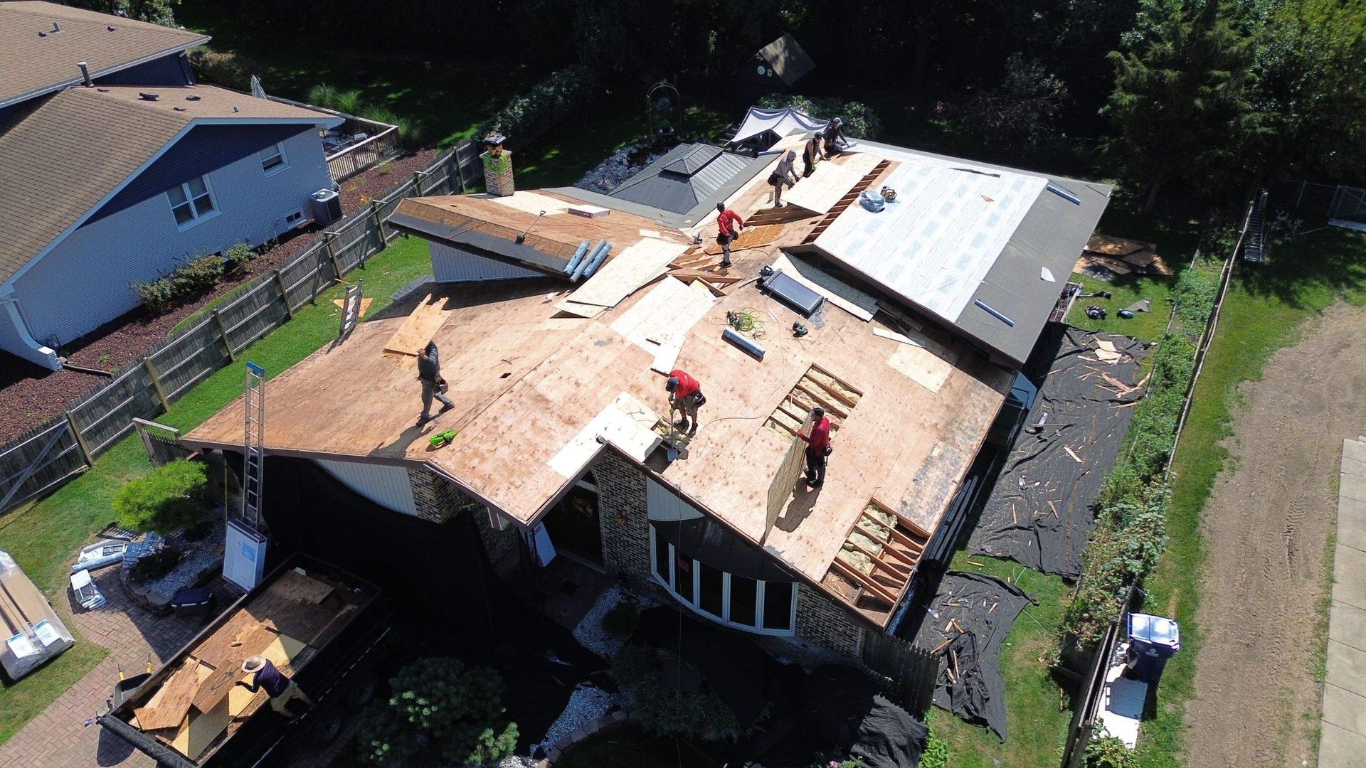 Roofers working on a residential roof, boards and shingles visible. Aerial view.