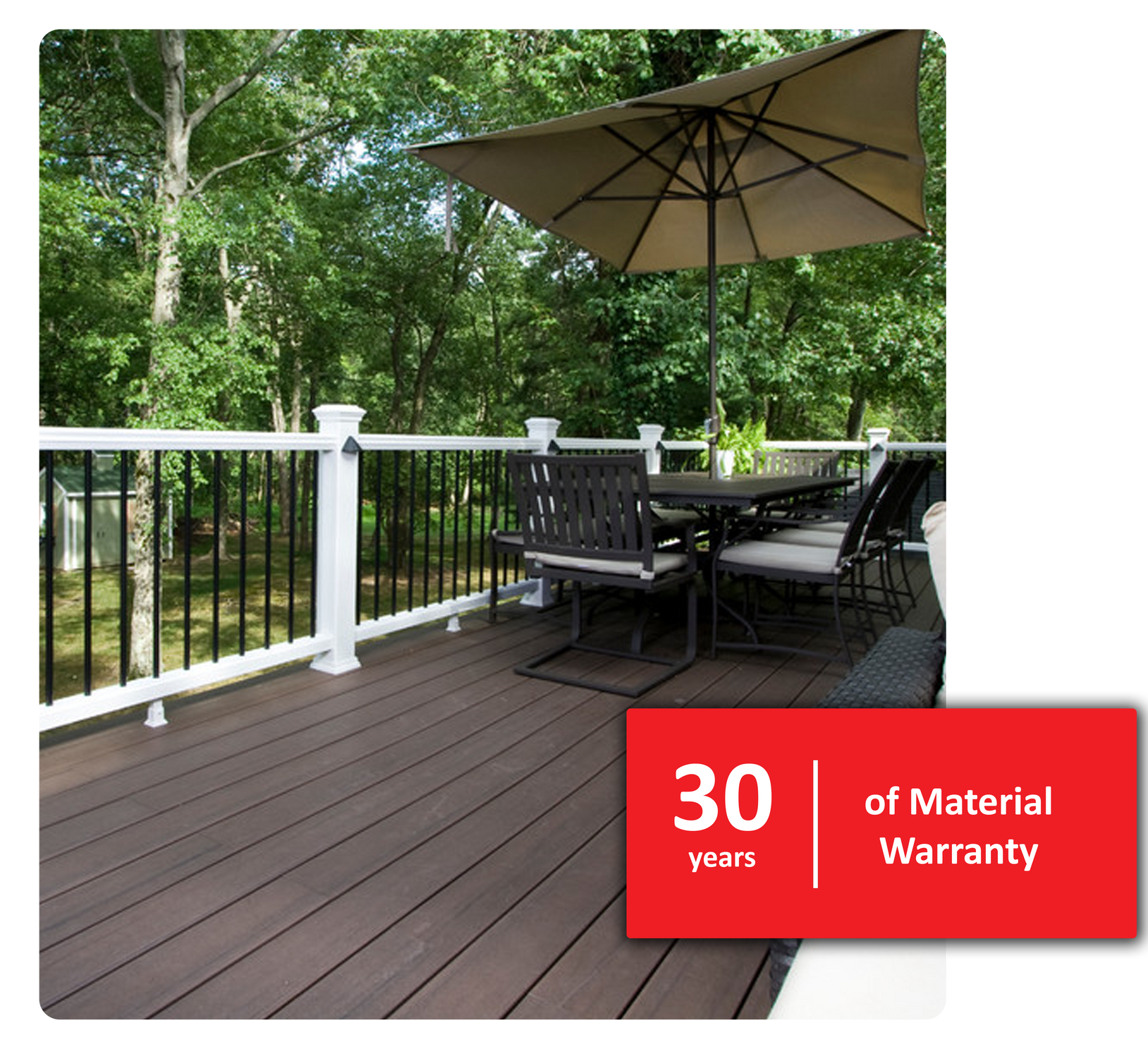 Wooden deck with outdoor furniture, umbrella, and white railing, set against a green tree backdrop. 