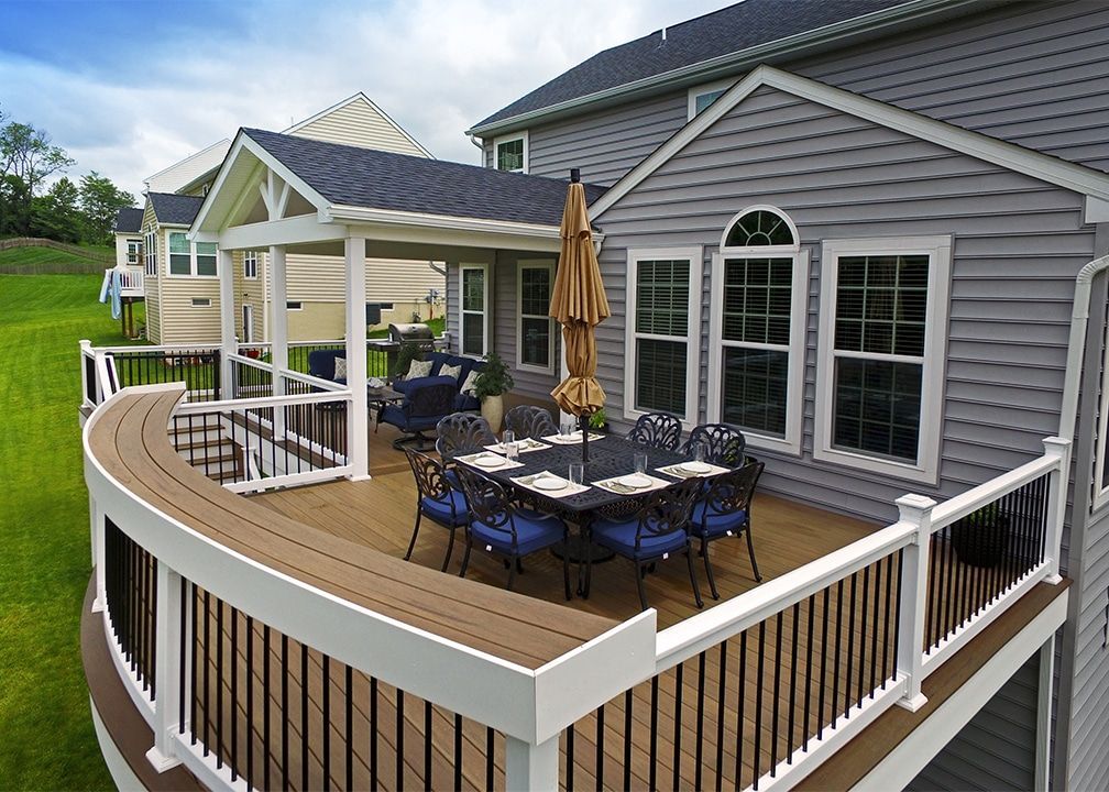 Wooden deck with furniture, umbrella, and partially covered seating area attached to a gray house.