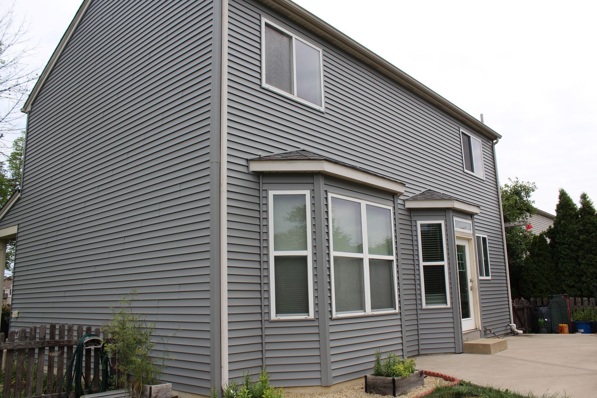 Gray two-story house with bay windows and siding, sitting on a concrete patio.